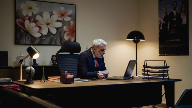 Senior businessman focused on laptop in modern office with stylish decor and artwork.