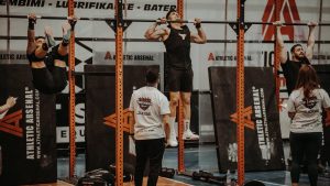 Athletes performing pull-ups in a CrossFit competition, judged by officials, showcasing strength and endurance.